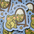 Am I the Drama sticker featuring a green frog looking at its reflection in a standing mirror on a blue background
