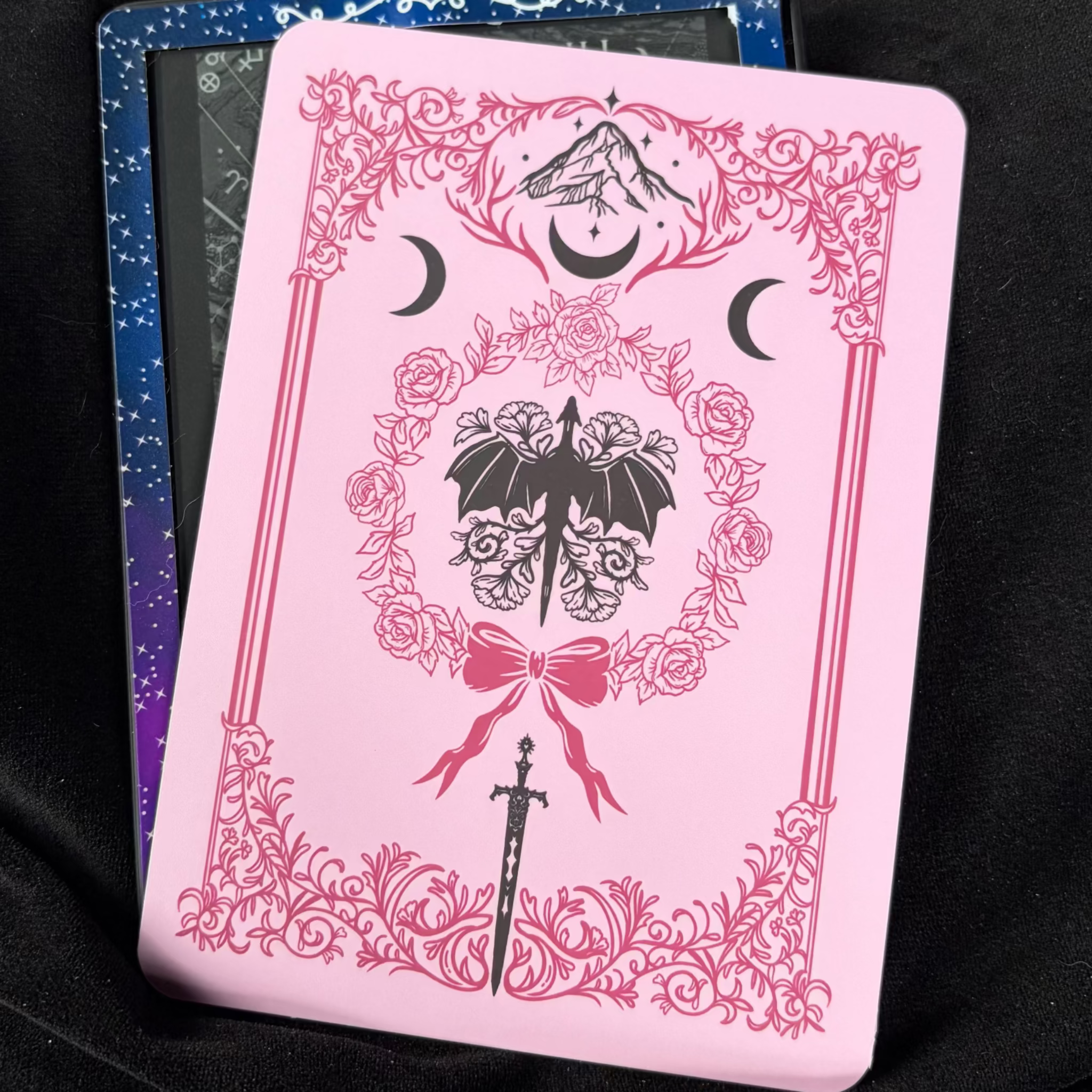 Pink romantasy Kindle backing insert with an ornate floral border, dark dragon, roses, crescent moons, mountains and sword
