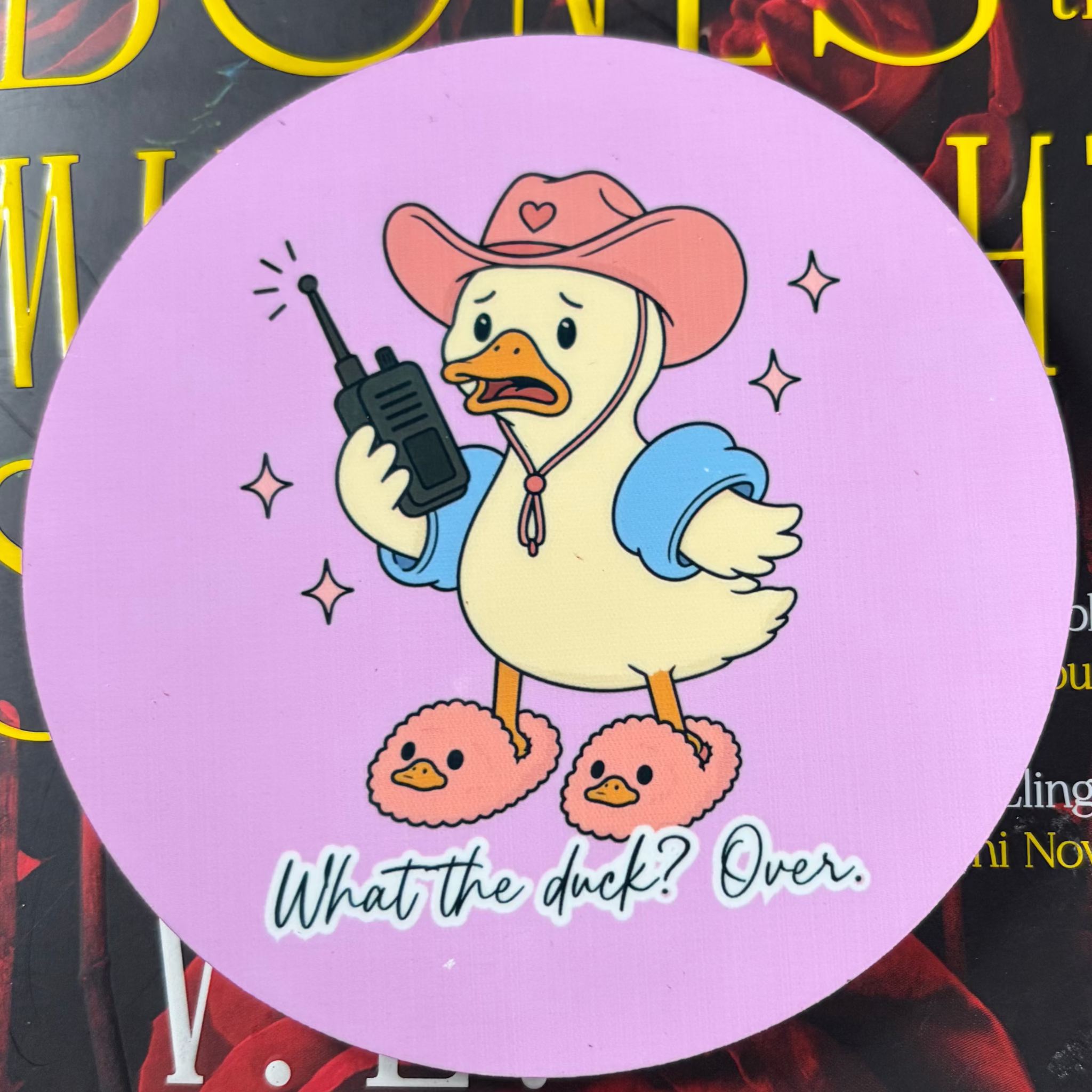 Round lilac coaster featuring a cartoon duck in a pink cowboy hat and fluffy slippers holding a walkie-talkie
