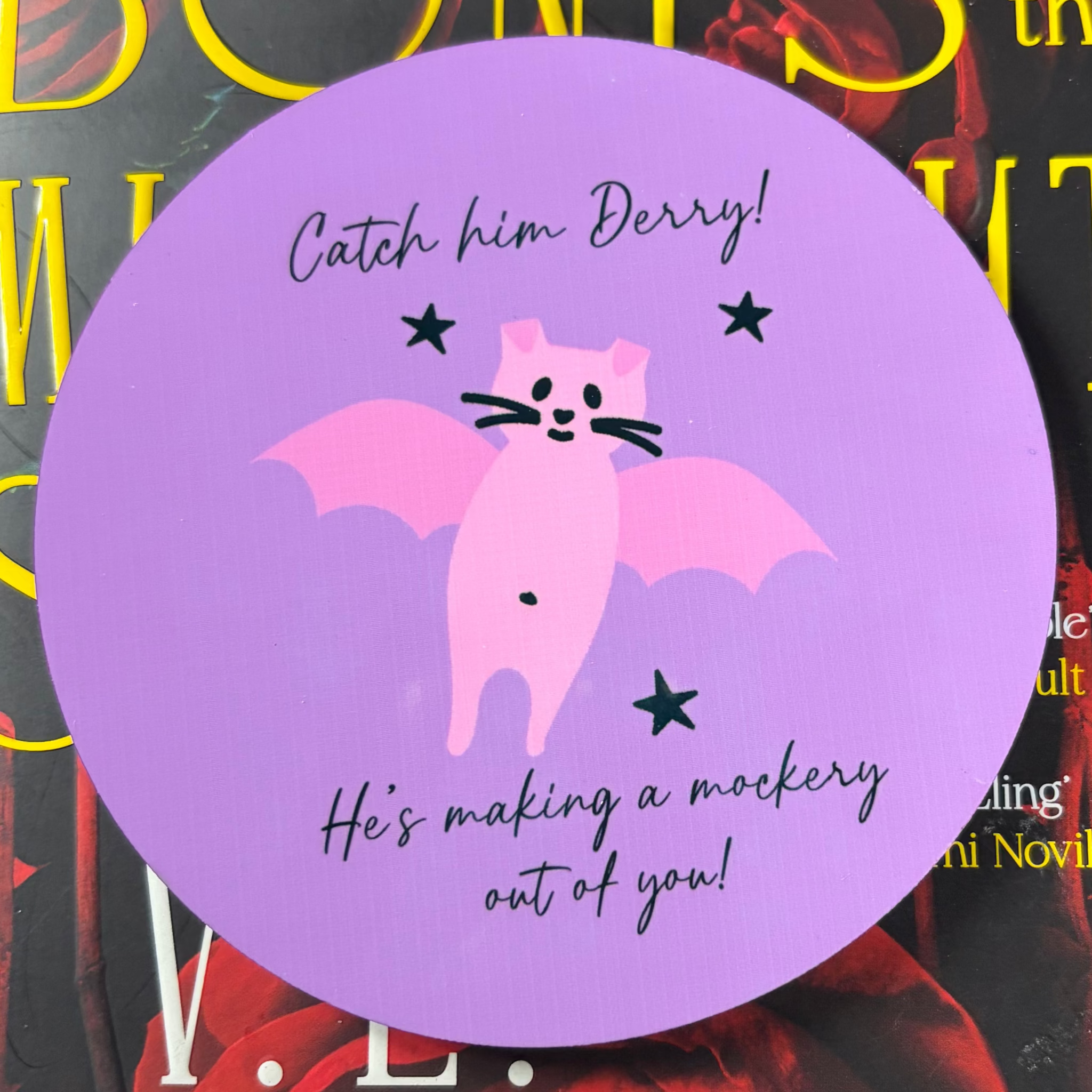 Round purple Catch Him Derry coaster featuring a funny pink bat and He’s Making a Mockery Out of You lettering
