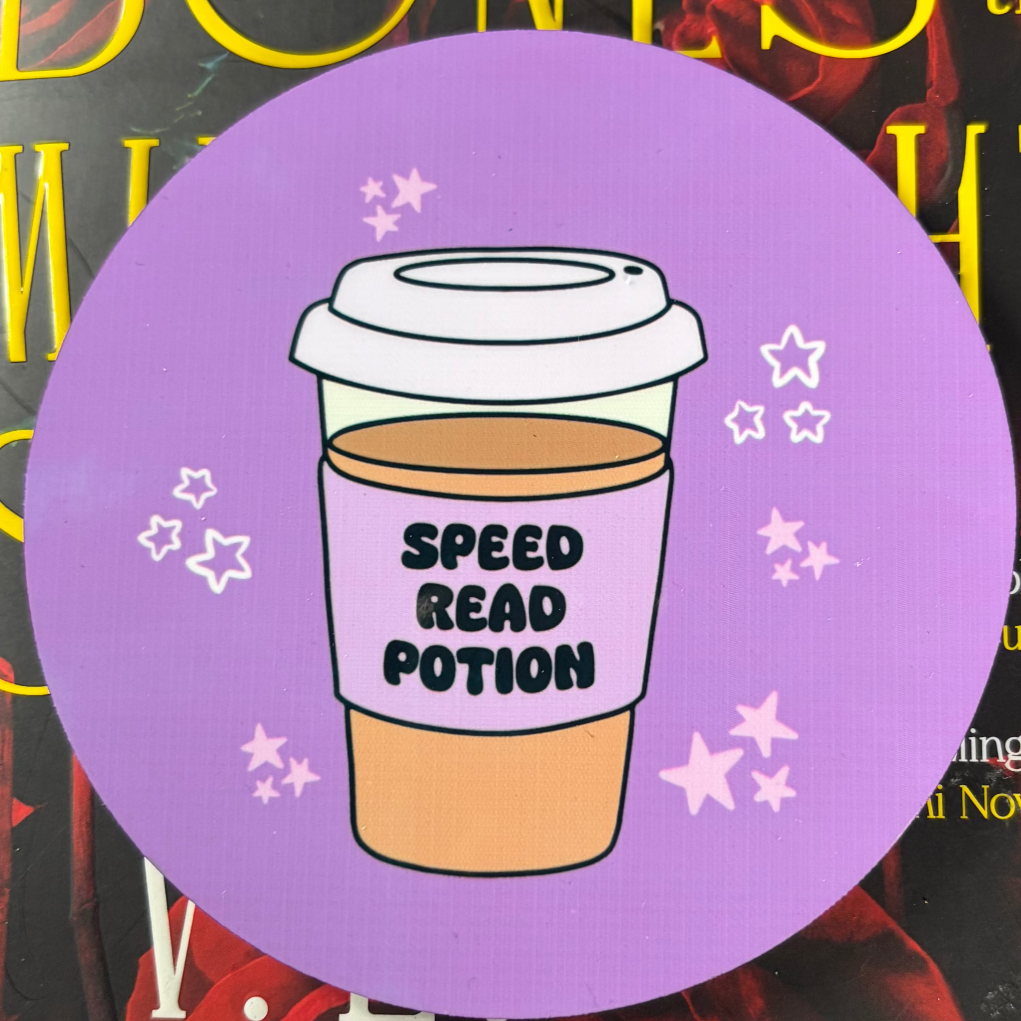 Round purple coaster featuring a takeaway coffee cup labelled Speed Read Potion, surrounded by pale pink and white stars
