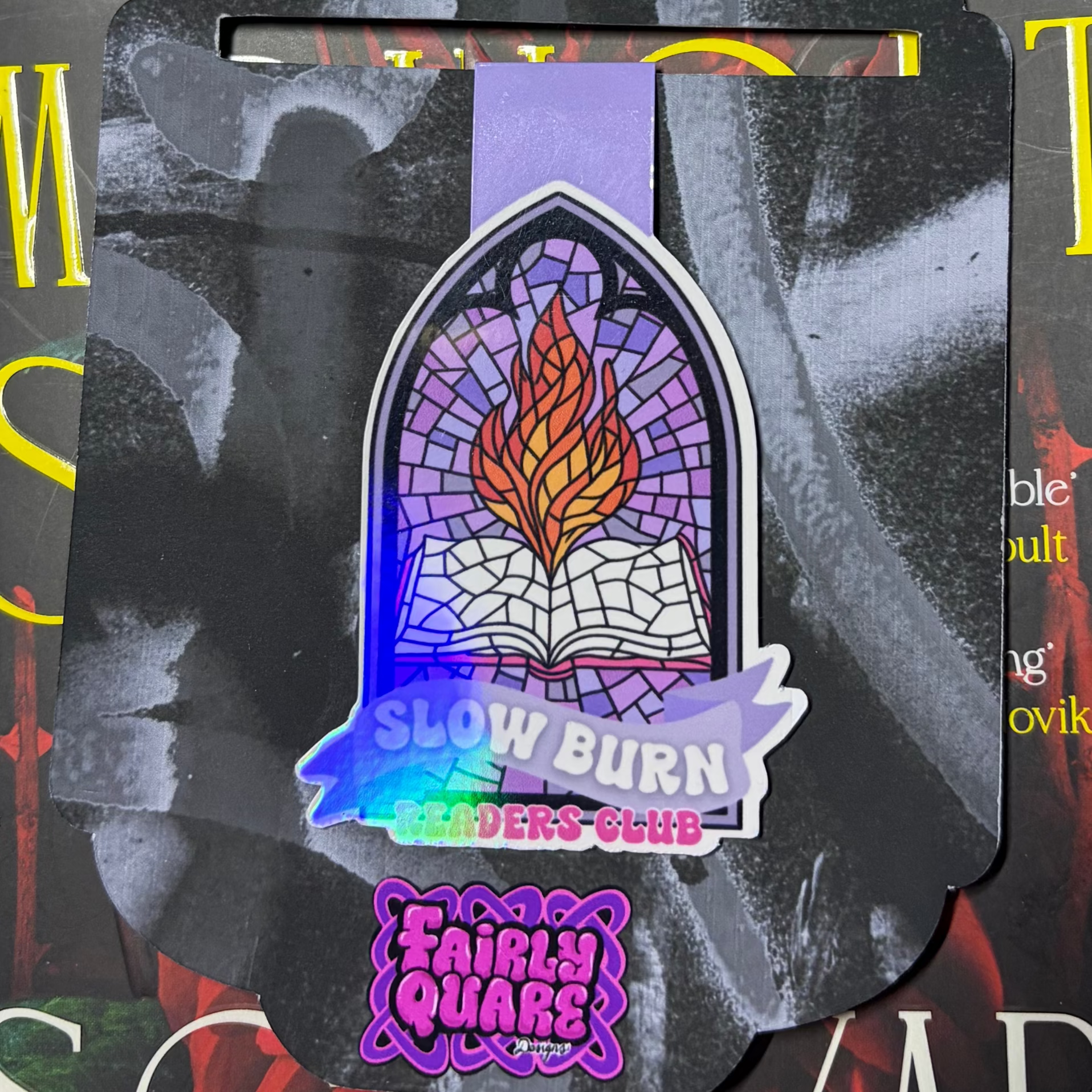 Holographic magnetic bookmark featuring a flaming open book inside a purple stained-glass window above the words Slow Burn Readers Club

