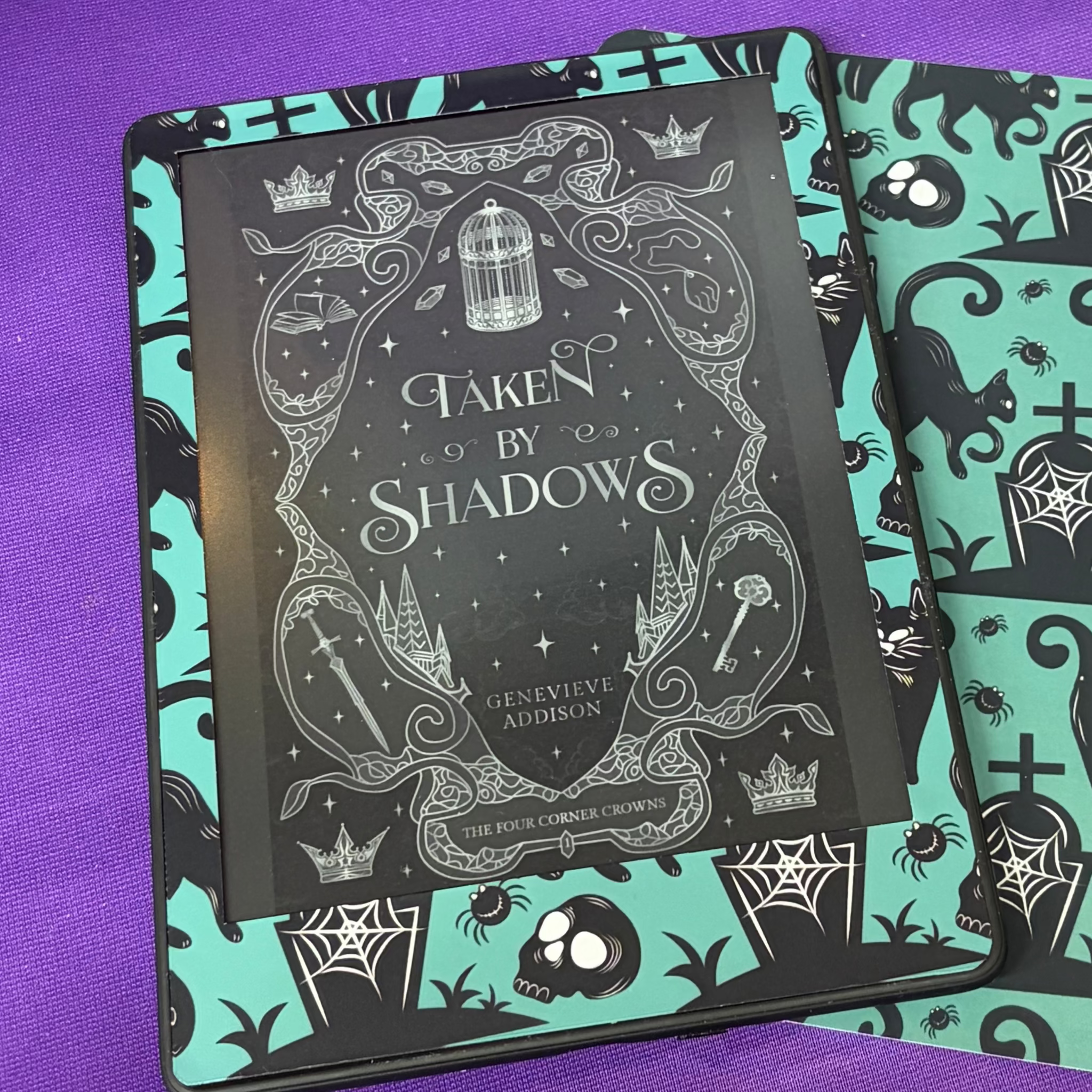 Teal and black Kindle front skin patterned with spooky cats, ghosts, skulls, gravestones, spiders and cobwebs
