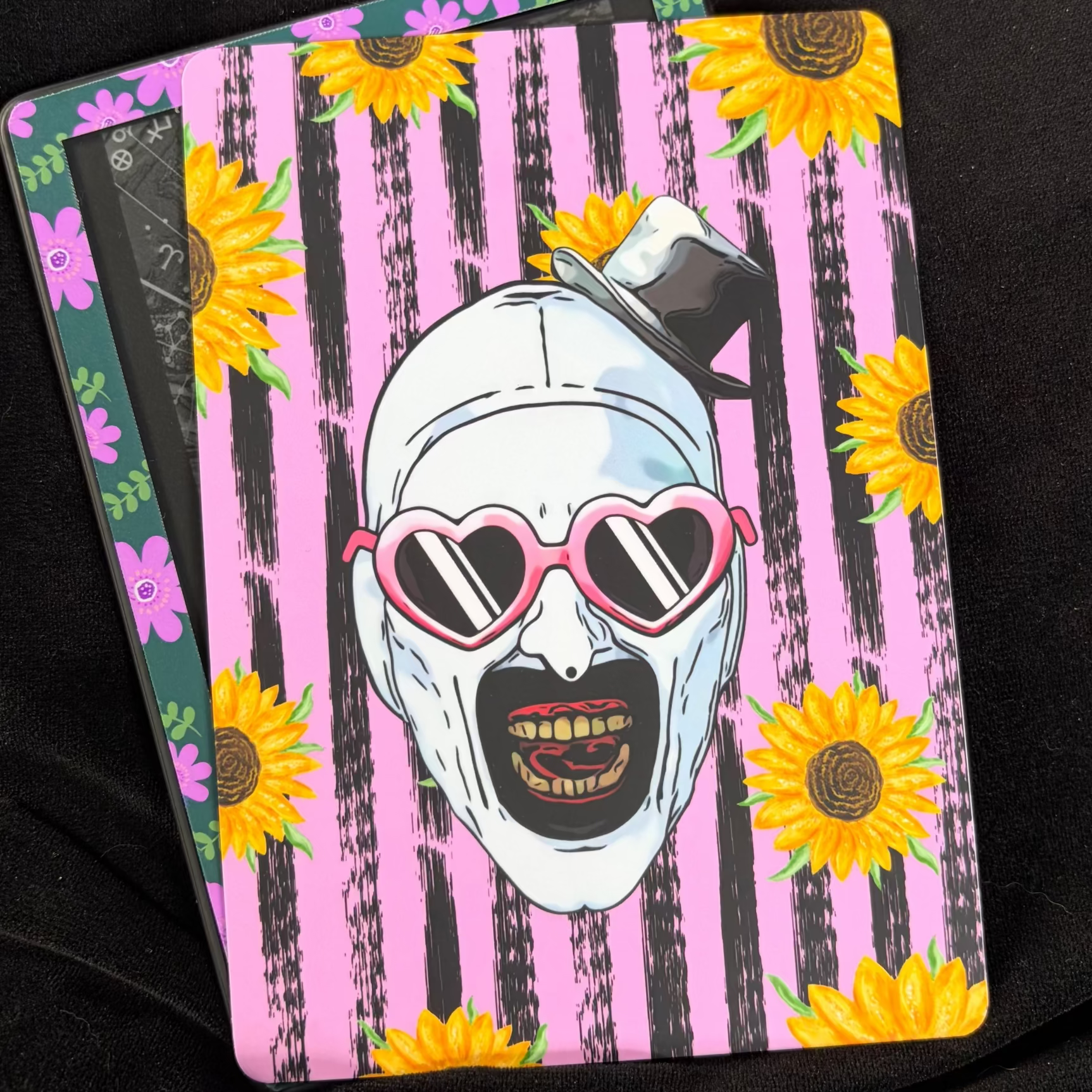 Terrifier-inspired Kindle backing insert featuring Art the Clown in pink heart sunglasses with black and pink stripes and yellow sunflowers

