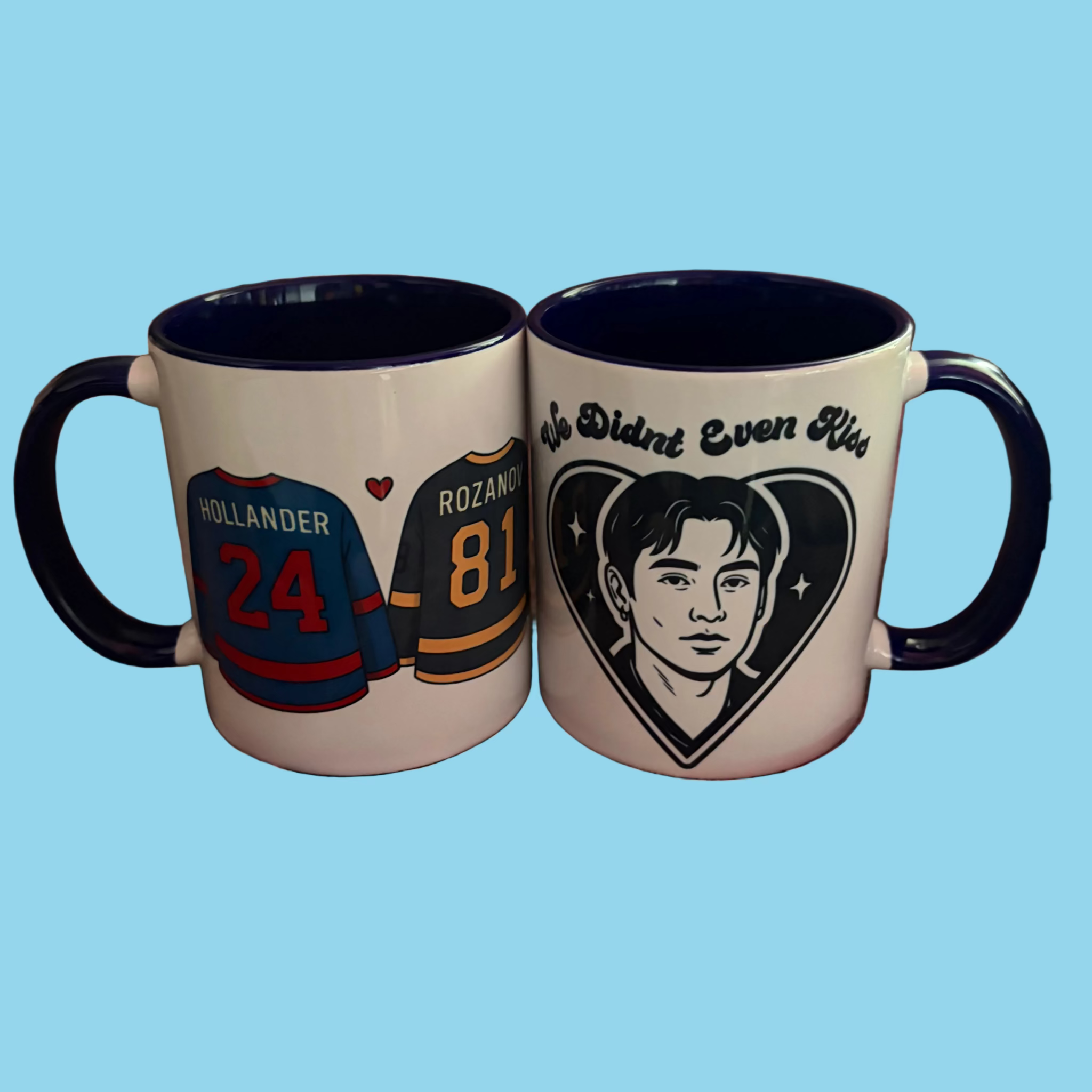 White ceramic mug with a dark blue interior and handle, featuring Shane Hollander and the quote We didn’t even kiss on one side and Hollander and Rozanov hockey jerseys on the other
