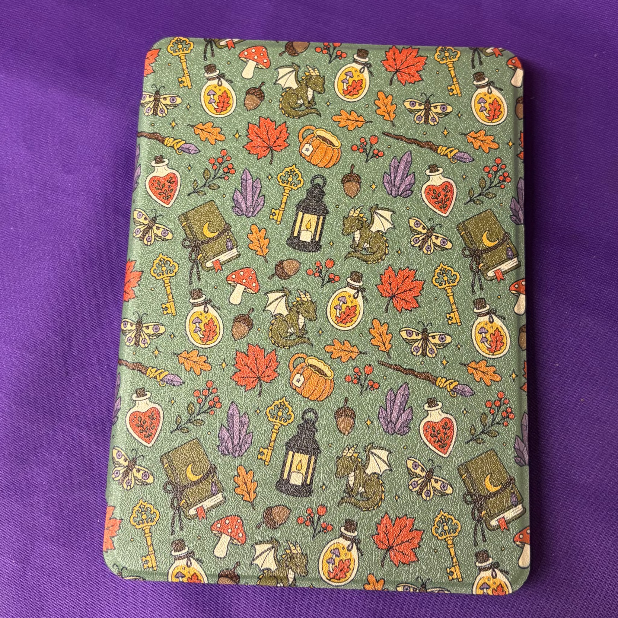 Green Witchy Woodland Autumn Kindle case patterned with mushrooms, leaves, potion bottles, books, moths and keys
