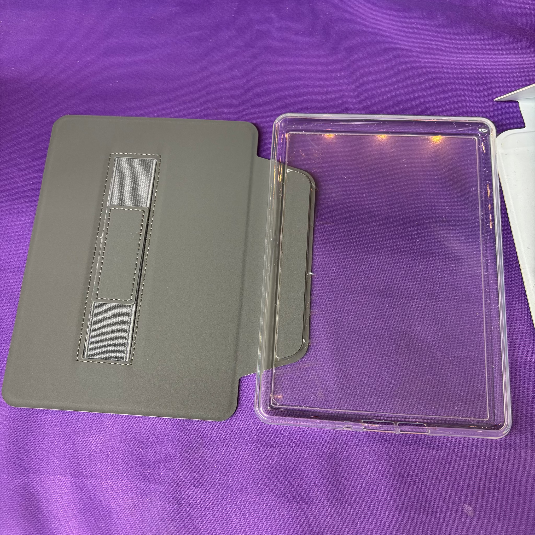 A gray tablet folio case with a clear protective cover placed on a purple fabric surface.