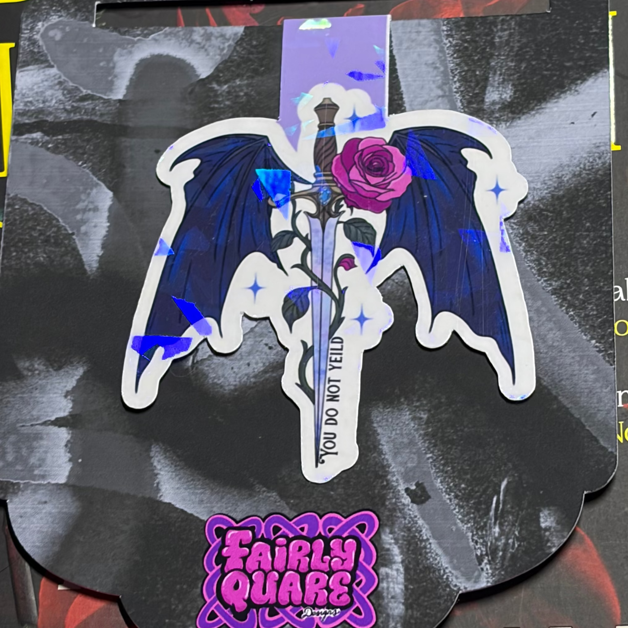 ACOTAR-inspired magnetic bookmark featuring a sword with dark wings, a purple rose and the words You Do Not Yield with shattered-glass holographic sparkle

