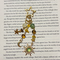 Golden Hour: Beaded gold Kindle charm with green, amber and cream stone beads, gold star, crescent moon and green sun charm on a star-shaped clasp, laid on an open book