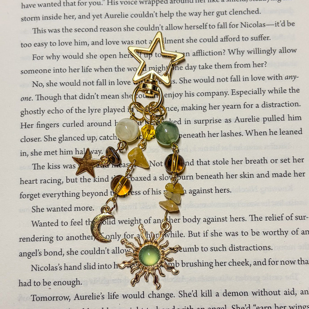 Golden Hour: Beaded gold Kindle charm with green, amber and cream stone beads, gold star, crescent moon and green sun charm on a star-shaped clasp, laid on an open book