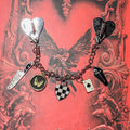 Morally Grey: Silver chain Kindle charm with two heart anchors, a Killing It knife, butterfly coin, checkered heart, ace of spades and coffin charms, on a red gothic book cover