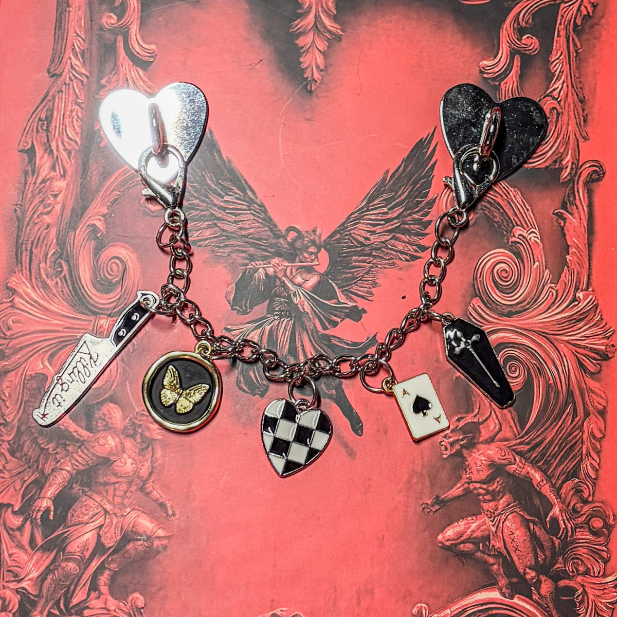 Morally Grey: Silver chain Kindle charm with two heart anchors, a Killing It knife, butterfly coin, checkered heart, ace of spades and coffin charms, on a red gothic book cover